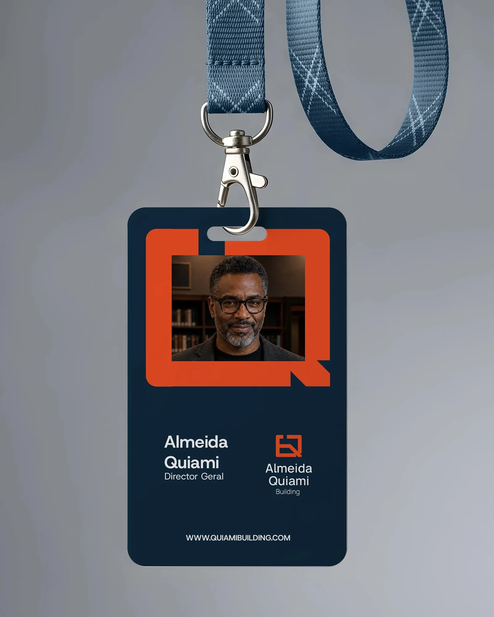 Almeida Quiami site ID badge on a lanyard — the director’s photo framed inside the orange monogram on navy