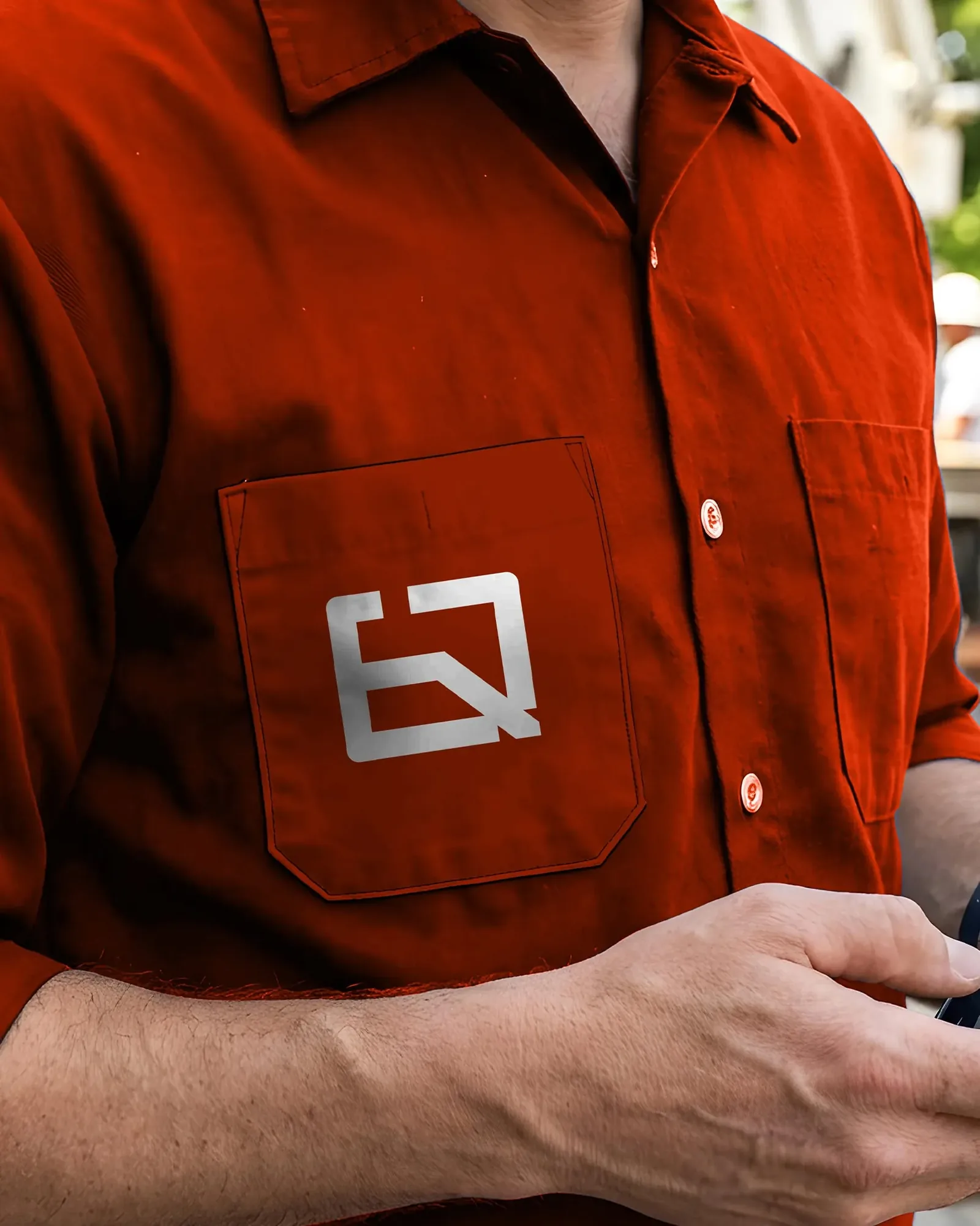 Almeida Quiami workwear — the white monogram printed on the chest pocket of an orange work shirt