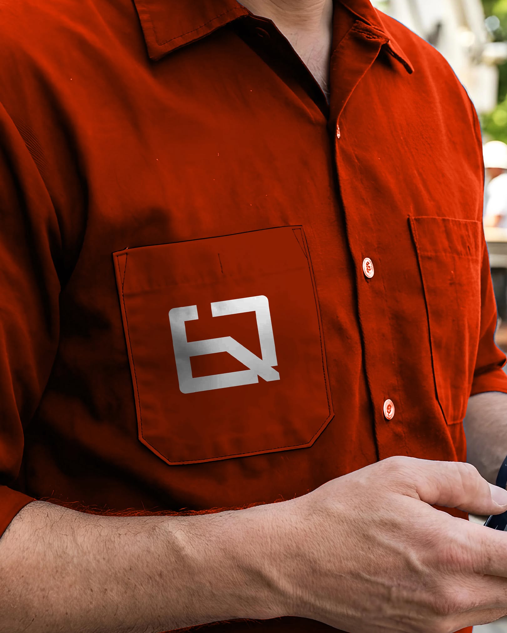 Almeida Quiami workwear — the white monogram printed on the chest pocket of an orange work shirt